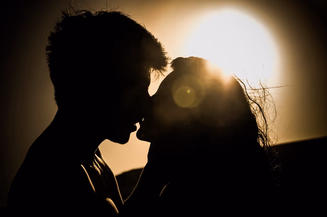 Silhouettes of couple kissing against sunset